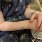 Little girl in a blue dress wearing a silver bracelet with cloud and rainbow charms
